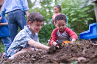 Two young boys playing in pile of dirt with trucs
