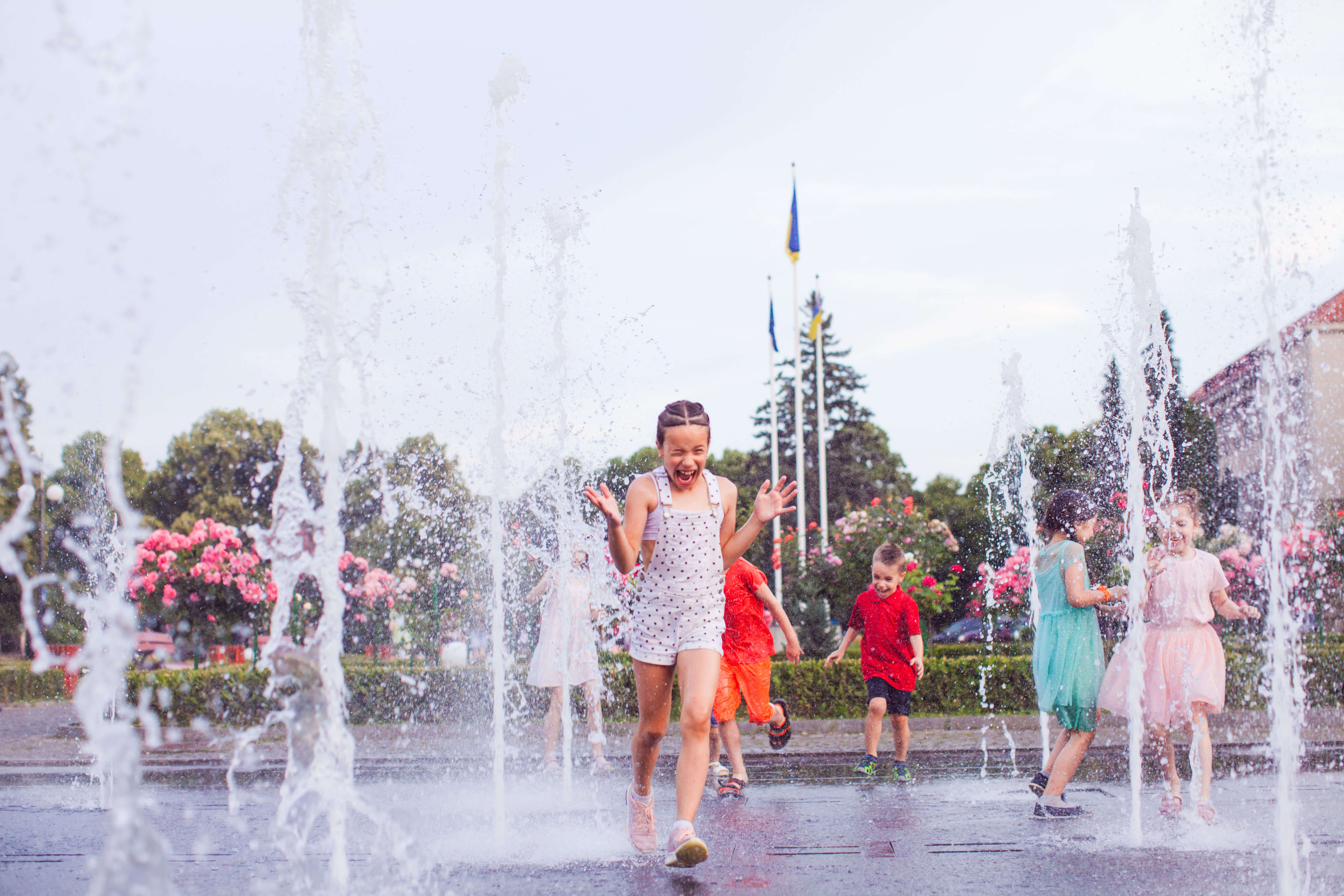 young children run through water at a splash pad in summer