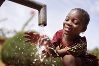 young girl washing hands under water spigot