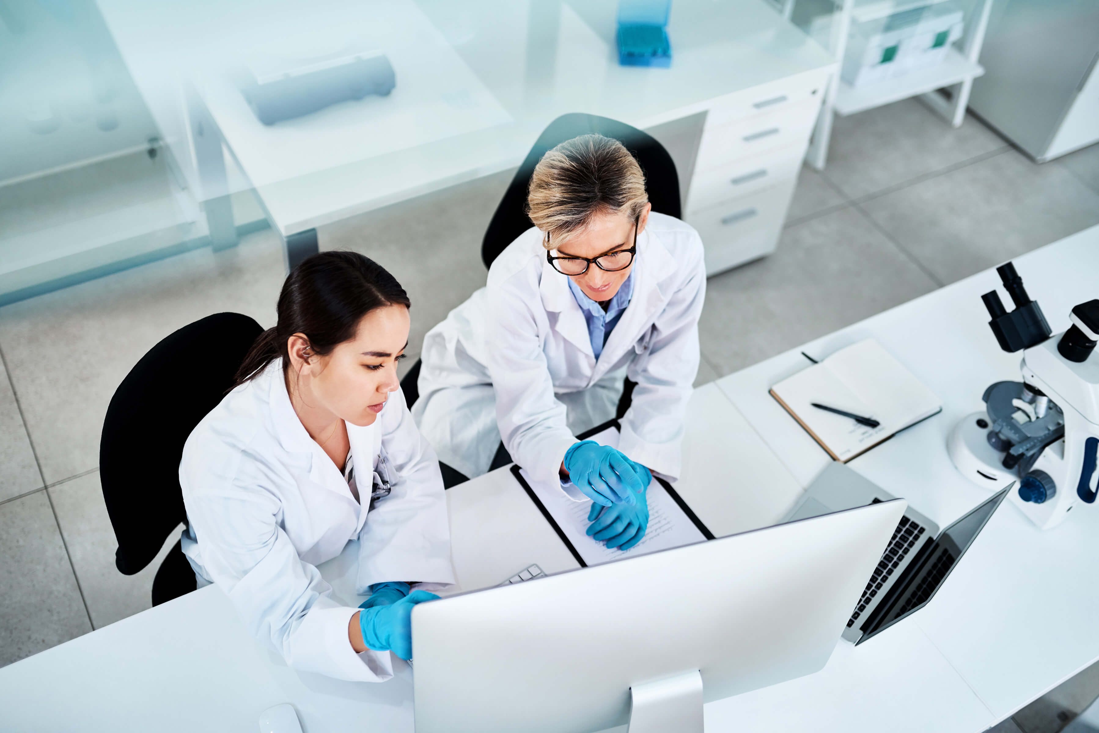two female scientists sit at a lab bench looking at a computer screen
