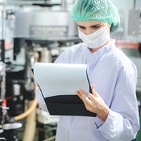 woman in a lab with hairnet and mask holding a clipboard